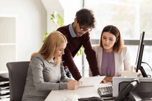 Three business professionals reviewing documents in a modern office, representing collaboration and planning, ideal for illustrating how tariff negotiations affect small business strategies.