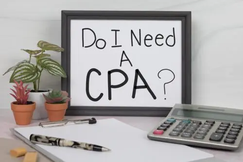 Desk with a framed sign asking 'Do I Need A CPA?' next to a calculator, pen, and notepad, symbolizing the contemplation of hiring a CPA for business financial management.