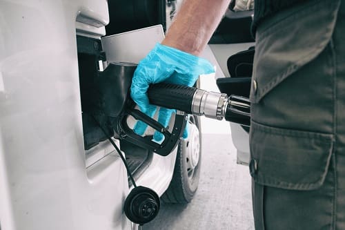 Coronavirus gas oil prices dropping man pumping gasoline at gas station wearing medical blue glove as COVID-19 spreading safety protection for touching germs.