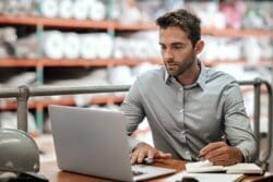 Warehouse manager taking notes and checking orders with a laptop