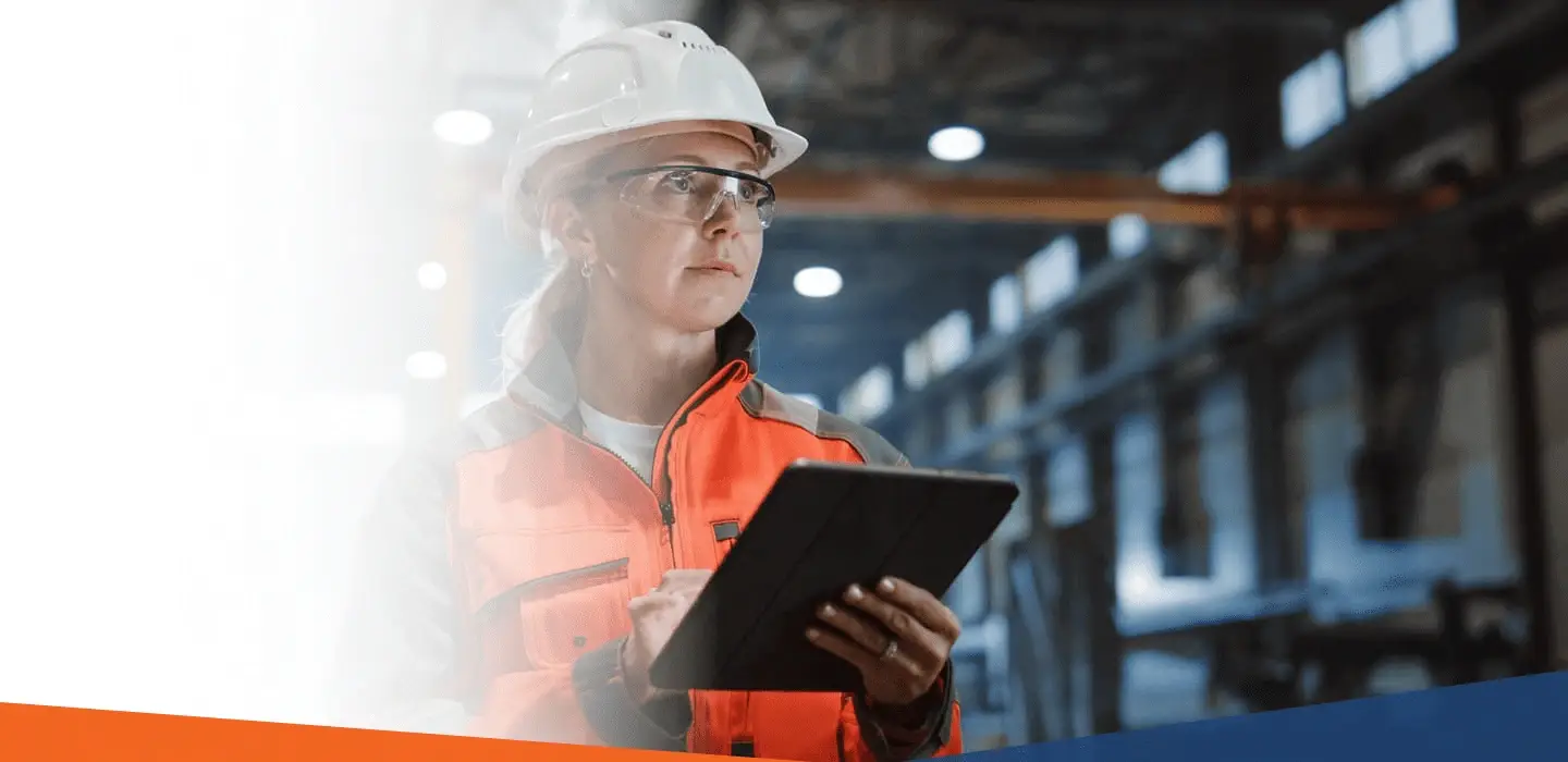 Female professional in safety gear using a tablet in an industrial facility.