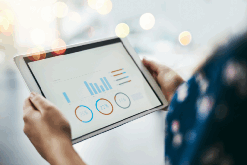 Businesswoman reviewing metrics for businesses using invoice factoring on a tablet with financial charts, bar graphs, and percentage data.